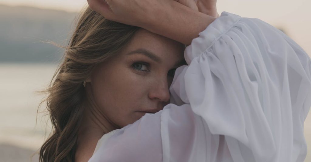 A woman in a white dress poses gracefully with a scenic sunset in the background.