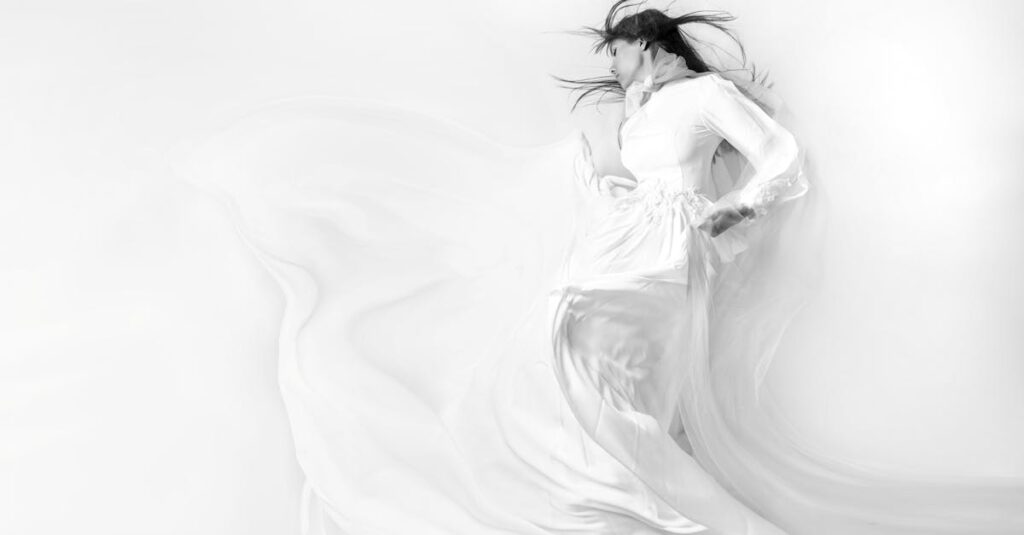 Elegant black and white photo of a woman in a flowing white dress, eyes closed.