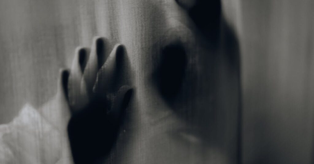 Blurred hands pressed against a curtain creating an eerie silhouette.