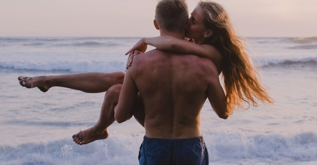 Romantic couple embracing at sunset on a beach, with waves crashing behind them.