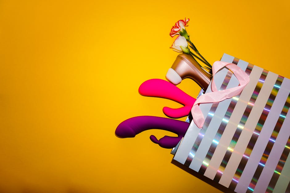Colorful vibrators with flowers in a holographic gift bag, set against a bold yellow background.